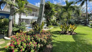 A lush garden with palm trees, a pool, and a two-story building with balconies. - Breathtaking Beachfront Apartment - FREE Wi-Fi (Bridgetown)