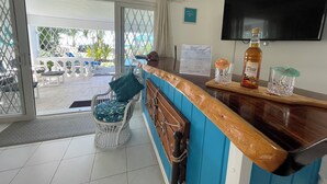 A reception area with a wooden counter, a television mounted on the wall, a signboard, and a view of the outdoor seating area. - Breathtaking Beachfront Apartment - FREE Wi-Fi (Bridgetown)