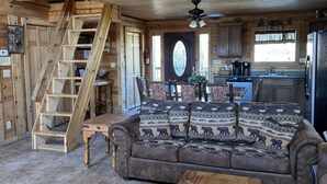 Un intérieur de cabine spacieux avec un plafond haut, un escalier en bois, un coin salon confortable avec un canapé et une table basse, et un espace cuisine.