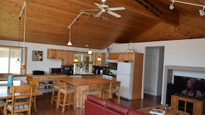 Amplia sala de estar con techo de madera, un sofá rojo, una mesa de comedor con sillas, una zona de cocina con armarios de madera y un televisor en una esquina.