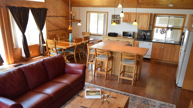 Un interior acogedor de cabaña con una mesa de comedor de madera, un sofá de cuero rojo y una zona de cocina con armarios y electrodomésticos de madera.