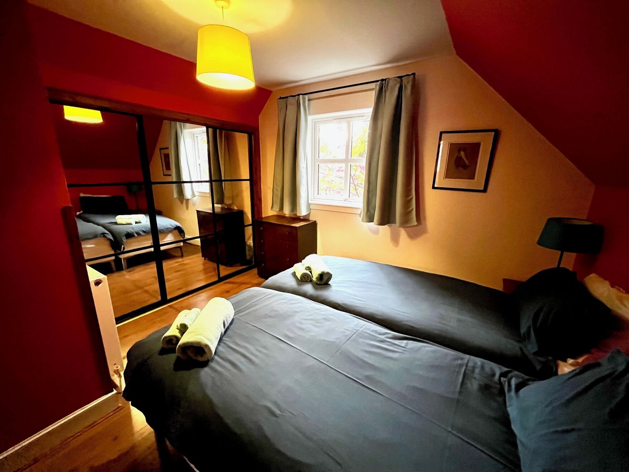 A bedroom with a bed, a mirror, a window with curtains, and a lamp.
