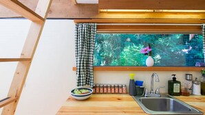 Una cocina con encimera de madera, un lavamanos, una ventana con vistas a la vegetación y un cuenco de fruta.