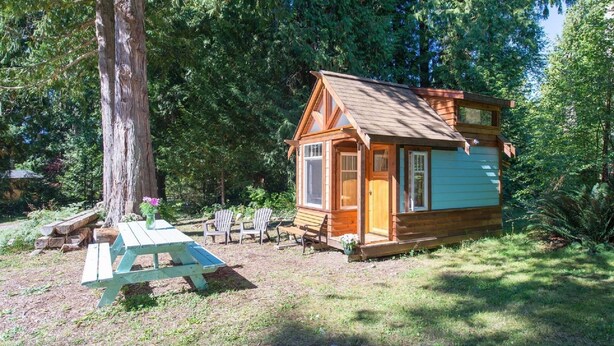 Una pequeña cabaña de madera con un porche, rodeada de árboles.