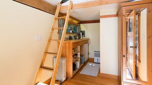 Una habitación pequeña con una escalera de madera que sube a una zona elevada, un radiador y un armario con puertas de cristal.