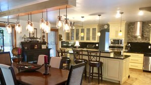A modern kitchen with a central island, pendant lighting, and a dining area with chairs and a table.