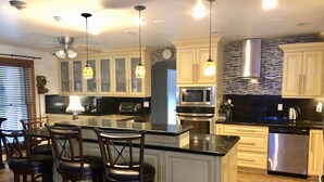 A modern kitchen with a central island, bar stools, stainless steel appliances, and a clock on the wall.