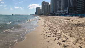 A beach with a pier in the background, sandy shore, and tall buildings.