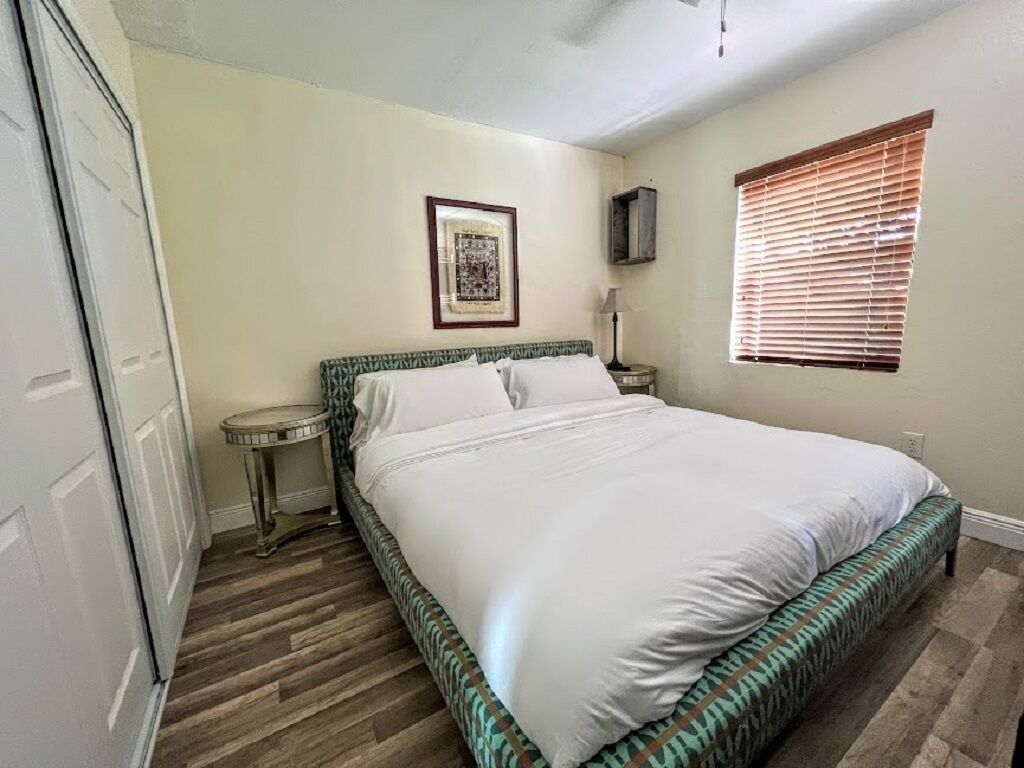 Un dormitorio con cama, mesita de noche, un cuadro enmarcado en la pared y una ventana con persianas.