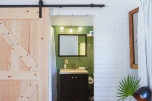 Een badkamer met een houten deur, groene tegels, een wastafel en een spiegel.