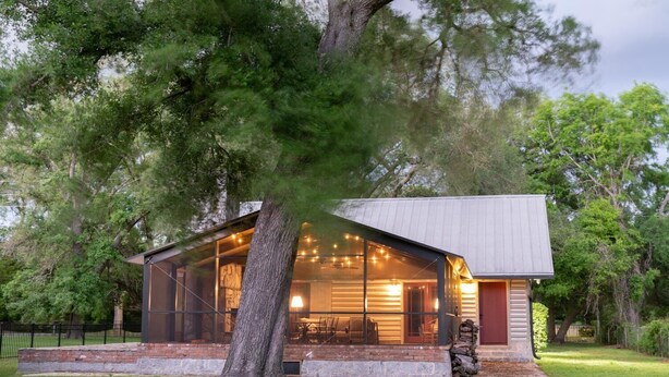 A modern house with a large glass front, a stone base, and a tree in front. - On the Beach, Teddy Roosevelt Stayed Here. Pet friendly, large fenced property (Pass Christian)