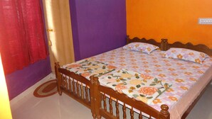 A bedroom with a wooden bed, floral bedding, a red curtain, and a purple and orange wall. - For Delightful stay visit us. (Madikeri)