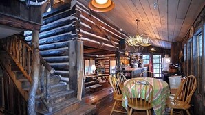 Un interior rústico con una escalera de madera, una mesa redonda de comedor con sillas y una araña.