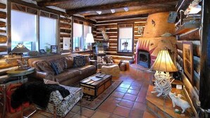 Interior de una cabaña de troncos con chimenea, sofá de cuero y decoración rústica.