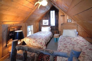 Une chambre mansardée chaleureuse avec deux lits, des murs en bois, un plafond en pente et une petite fenêtre.