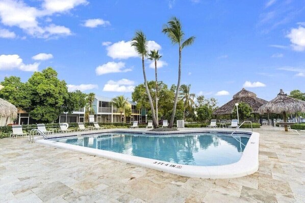 A swimming pool with lounge chairs, palm trees, and thatched-roof structures. - Key largo Kawama Villa N2 (Key Largo)