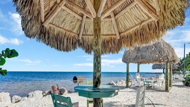 Une plage avec un parasol en chaume, une petite table ronde et deux chaises.