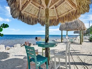 A beach setting with a thatched umbrella, a small round table, and two chairs. - Key largo Kawama Villa N2 (Key Largo)