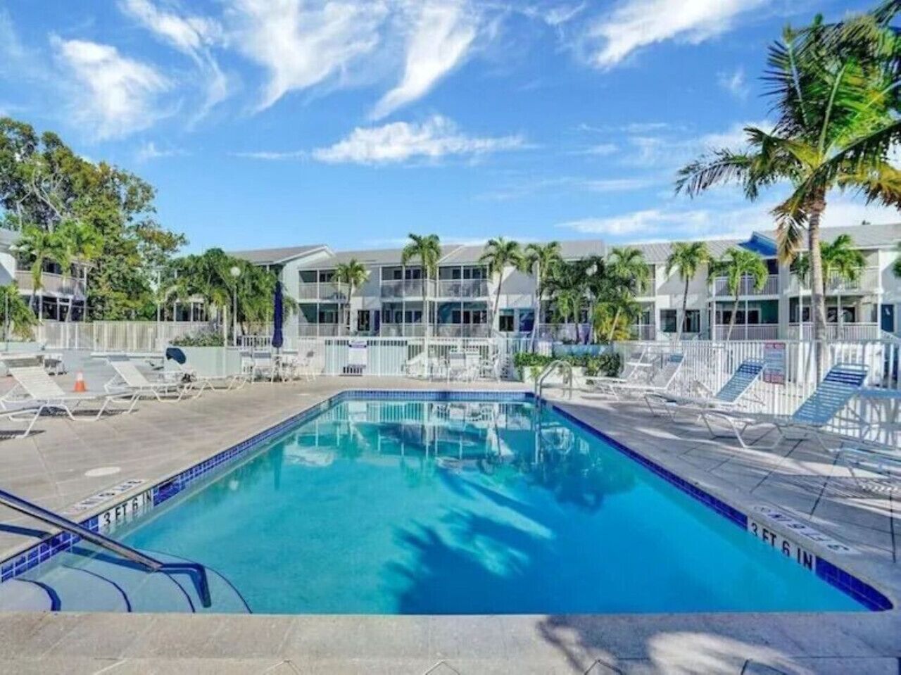 A swimming pool with lounge chairs, a building with multiple windows, and palm trees.