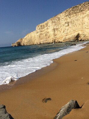 A beach with clear blue water, sandy shore, and a rocky cliff. - villa fully equipped with swimming pool and sea view and 360 ° (kamilari)