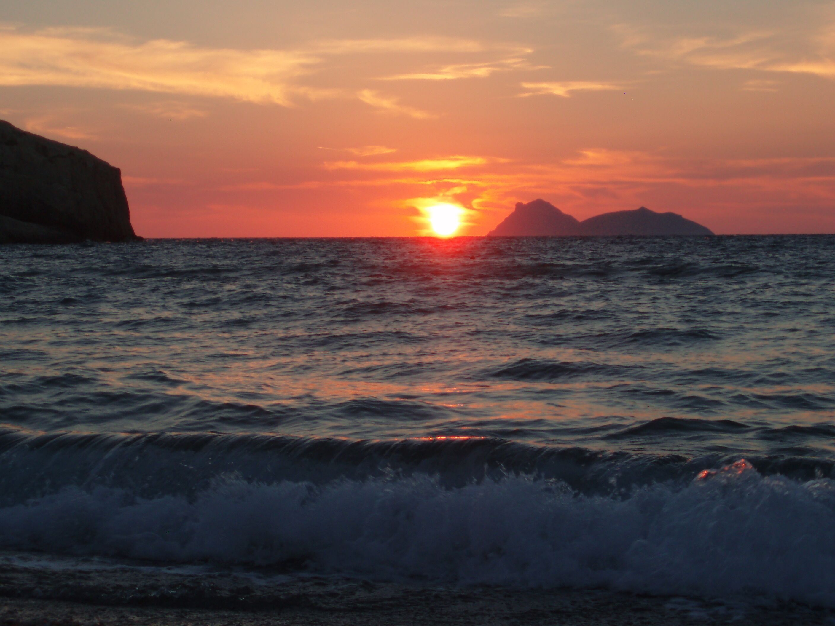 Ein Sonnenuntergang über dem Meer mit brechenden Wellen an der Küste.