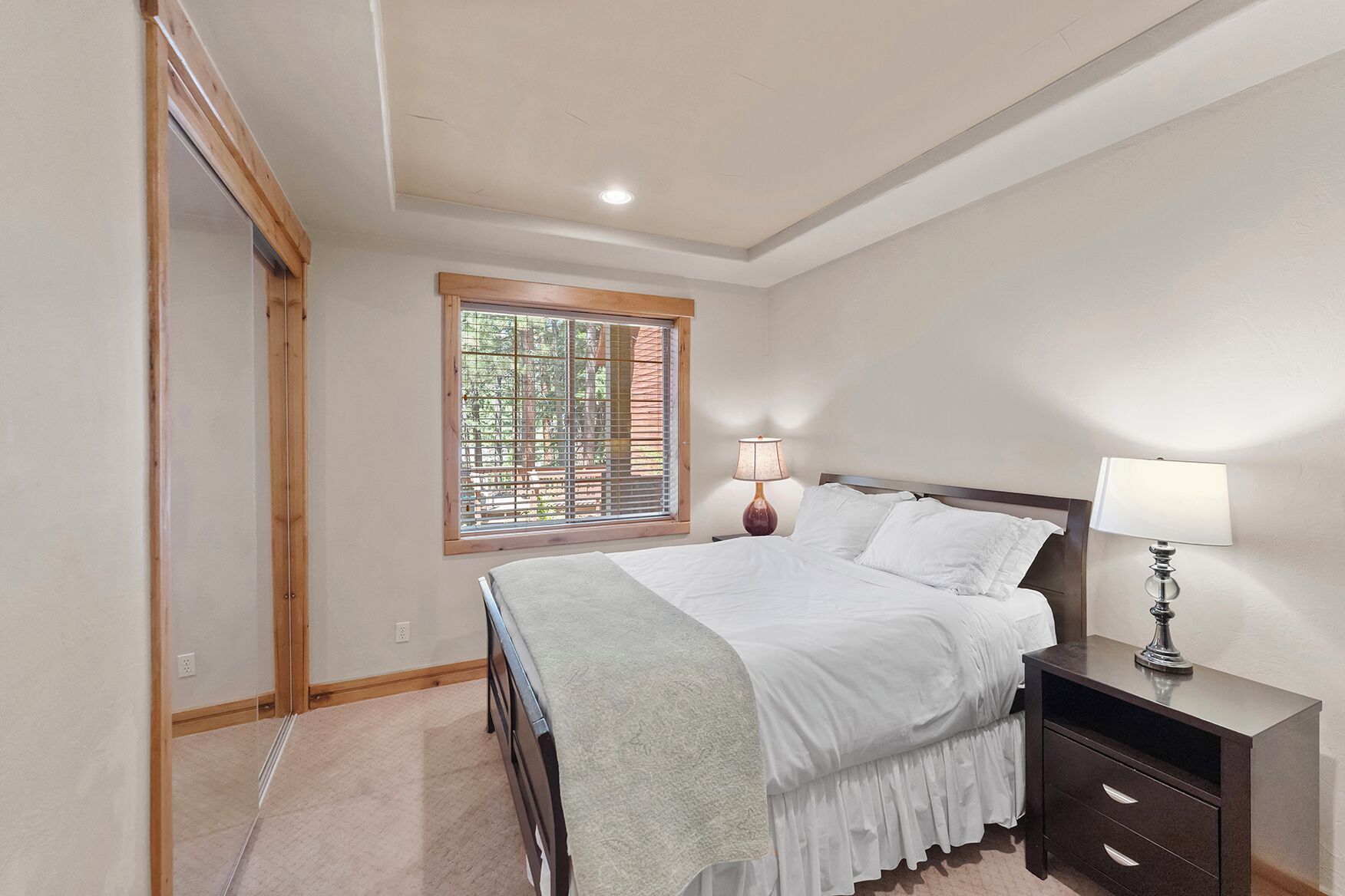 A bedroom with a bed, bedside lamps, a window with blinds, and a wooden door.