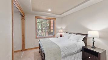 A bedroom with a bed, bedside lamps, a window with blinds, and a wooden door.