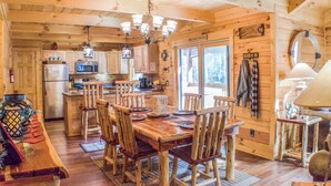 A wooden cabin with a dining area, kitchen, and a large window. - True Log Cabin 3/2 Fiber OPTICS, Trout-Stocked Creek, Hot Tub ! (Deep Gap)