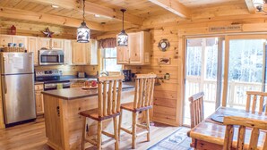 A wooden cabin kitchen with a refrigerator, microwave, stove, and wooden bar stools. - True Log Cabin 3/2 Fiber OPTICS, Trout-Stocked Creek, Hot Tub ! (Deep Gap)