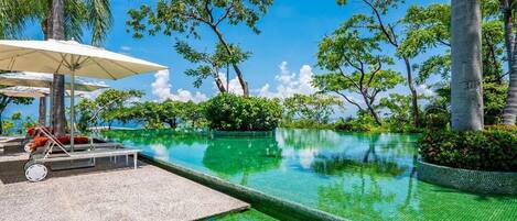 Céu azul límpido, piscina com borda azulejada e espreguiçadeiras com guarda-sóis.