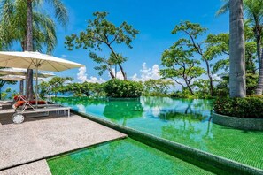 A clear blue sky, a swimming pool with a tiled edge, and lounge chairs with umbrellas.