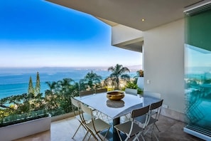 A balcony with a table and chairs, overlooking a coastal landscape.