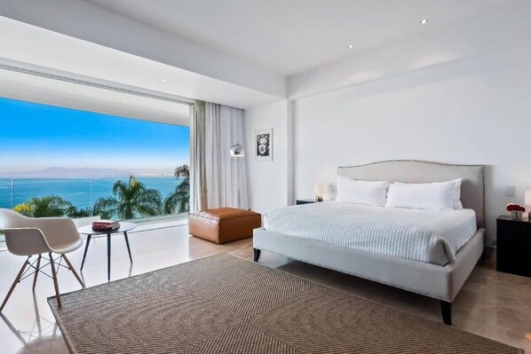 Un dormitorio moderno con una cama grande, vistas al océano y un balcón con una silla y una mesa.