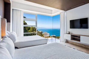 A modern hotel room with two beds, a TV, and a balcony with a view of the sea.