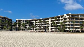 Hotel a primera línia de platja amb múltiples balcons, palmeres i un cel blau clar.