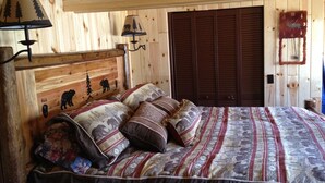 A wooden cabin bedroom with a bed, two wall-mounted lamps, a headboard with animal carvings, and a wooden door.