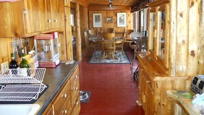 A wooden cabin interior with a kitchen area featuring wooden cabinets, a dining table, and a bar area.