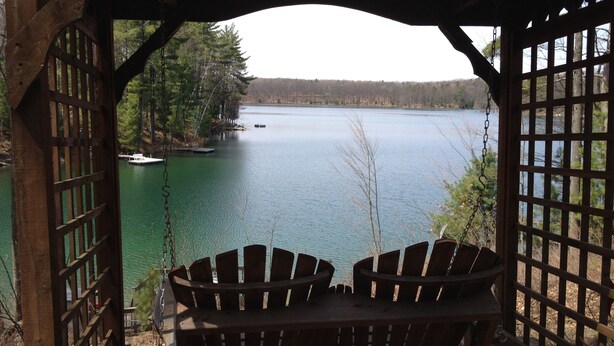 A wooden gazebo with two Adirondack chairs overlooking a lake.