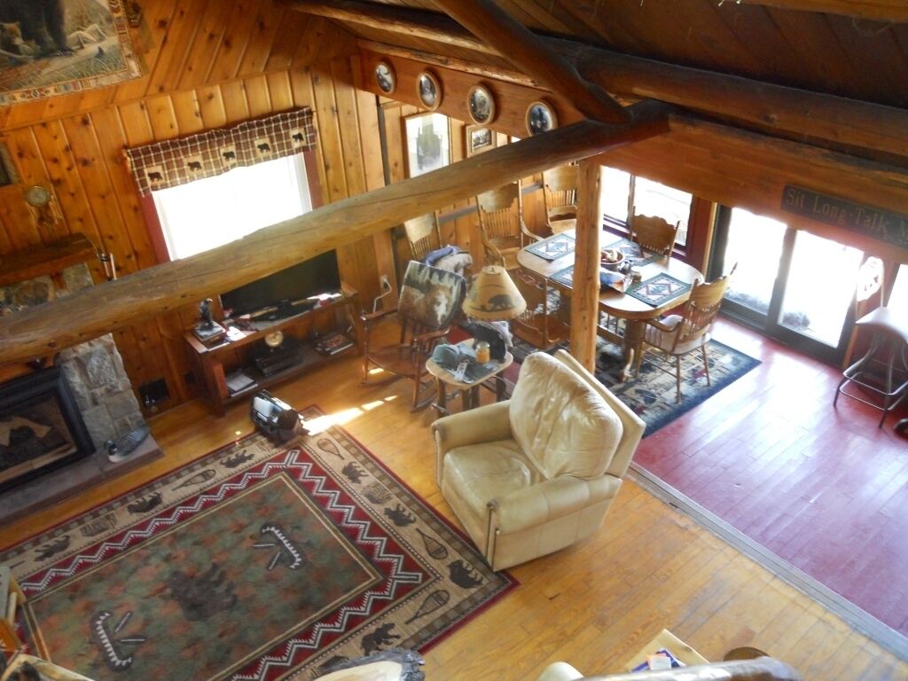 A rustic cabin interior with a fireplace, leather armchair, dining table, and a view of the outside.