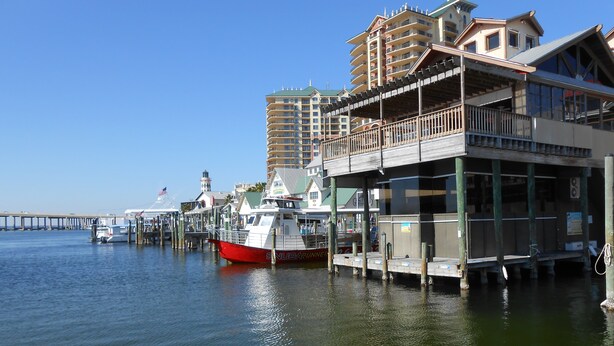 A waterfront hotel with a dock, a red boat moored at the pier, and a lighthouse in the background. - SUNDIAL COTTAGE: CRYSTAL BEACH, DESTIN, FL.  PRIVATE POOL!     (Destin)