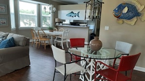 A dining area with a glass table surrounded by red and white chairs, a kitchen in the background, and a fish mural on the wall. - SUNDIAL COTTAGE: CRYSTAL BEACH, DESTIN, FL.  PRIVATE POOL!     (Destin)