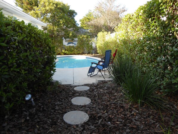 A backyard with a swimming pool, a blue chair, and a stepping stone path.