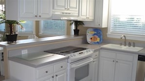 A kitchen with white cabinets, a stove, a sink, and a window with blinds. - SUNDIAL COTTAGE: CRYSTAL BEACH, DESTIN, FL.  PRIVATE POOL!     (Destin)