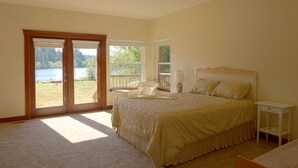 A bedroom with a large bed, a nightstand, a chair, and a view of a lake through a sliding glass door. - Close-in Beautiful Retreat: Large, Lodge-Like Private Lakefront Setting (Renton)