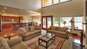 A spacious living area with a large sofa set, a coffee table, and a rug. There is a kitchen area with wooden cabinets and a dining area with chairs. - Close-in Beautiful Retreat: Large, Lodge-Like Private Lakefront Setting (Renton)