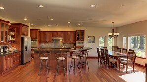 A spacious kitchen with wooden cabinets, a central island with bar stools, and a dining area with a large table and chairs. - Close-in Beautiful Retreat: Large, Lodge-Like Private Lakefront Setting (Renton)