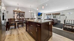 A modern kitchen with a large island, wooden chairs, and pendant lighting.
