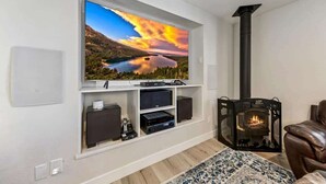 A living room with a mounted TV, a fireplace, and a mounted shelf with electronic devices.