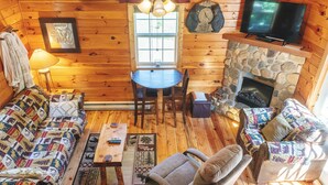 Un intérieur de chalet chaleureux avec une cheminée en pierre, des murs en bois, un téléviseur et un canapé matelassé.