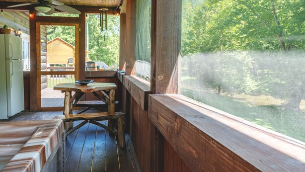 Une terrasse en bois avec une table et des bancs, donnant sur une cour clôturée et arborée.